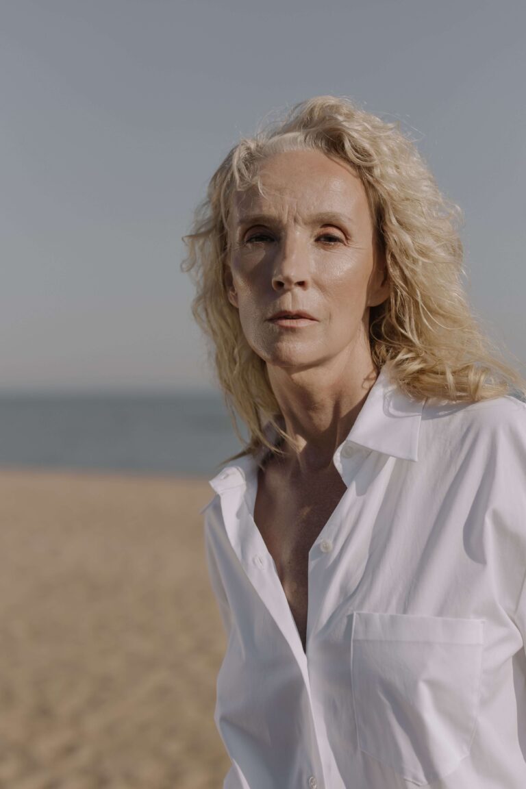 A mature blonde woman over 60 with visible facial wrinkles standing outdoors in natural sunlight while exploring aging face skin problems treatment options